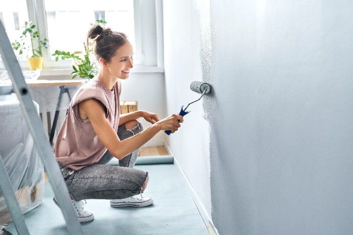 Eine Frau streicht eine Zimmerwand mit grauer Strukturfarbe.